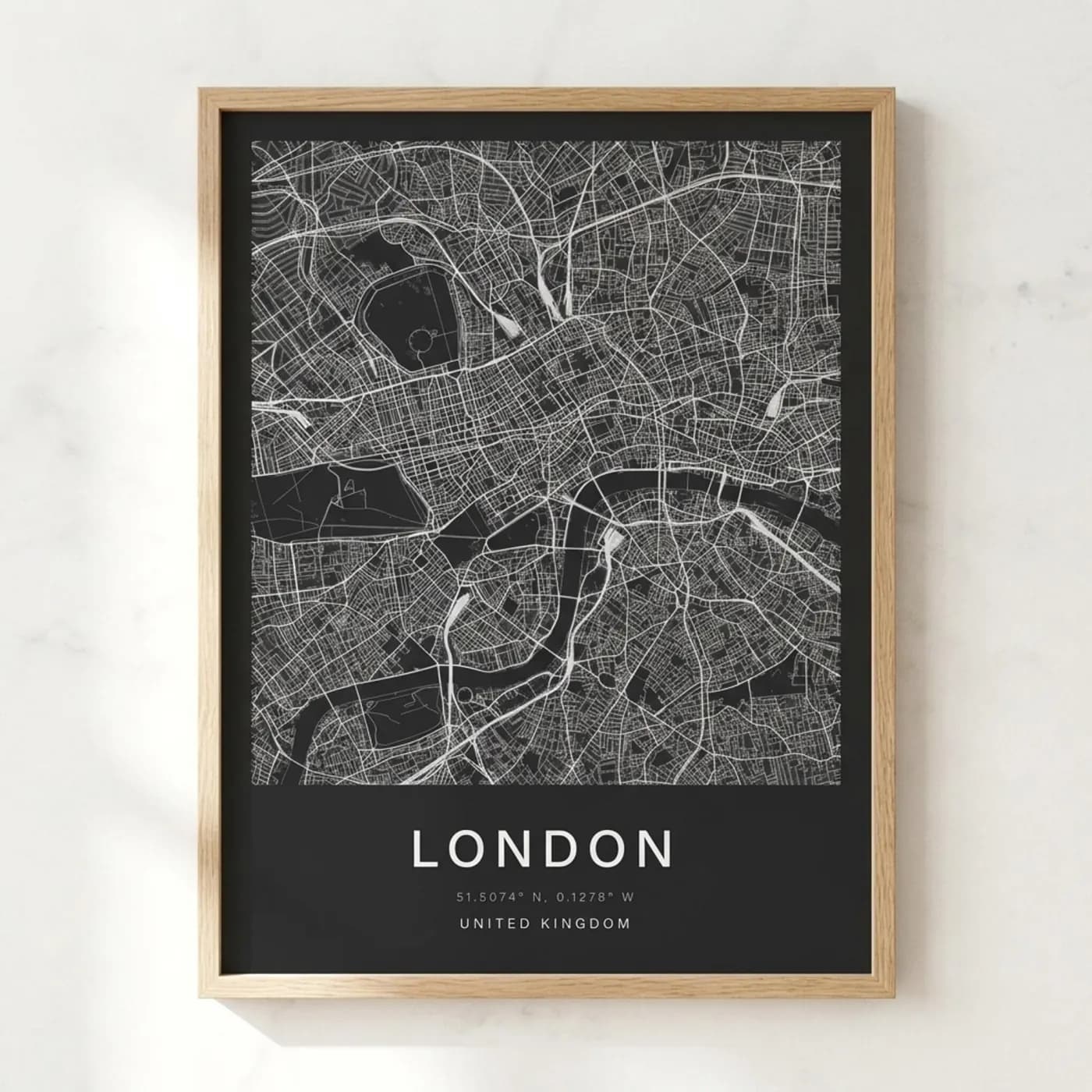 Oak-framed London street map poster, white roads on charcoal, hung on a white marble wall