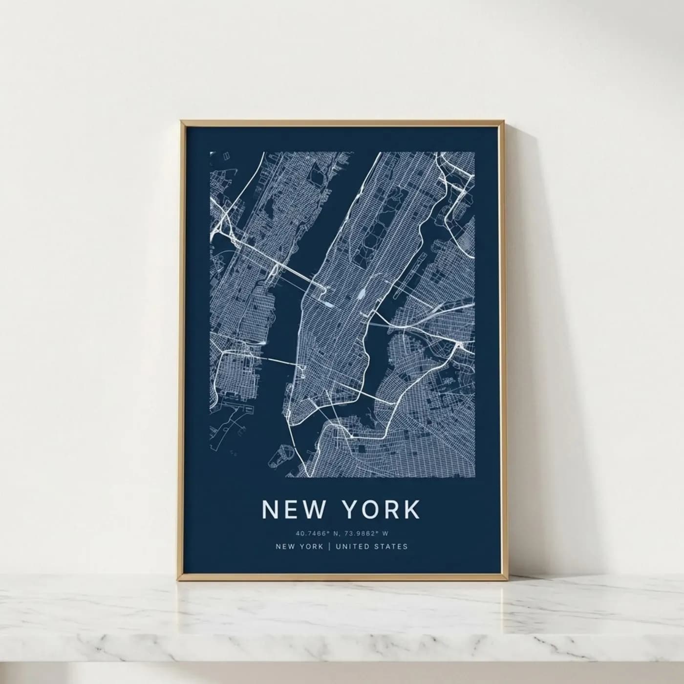 Gold-framed New York street map poster, white lines on navy blue, leaning on a marble shelf against a pale wall